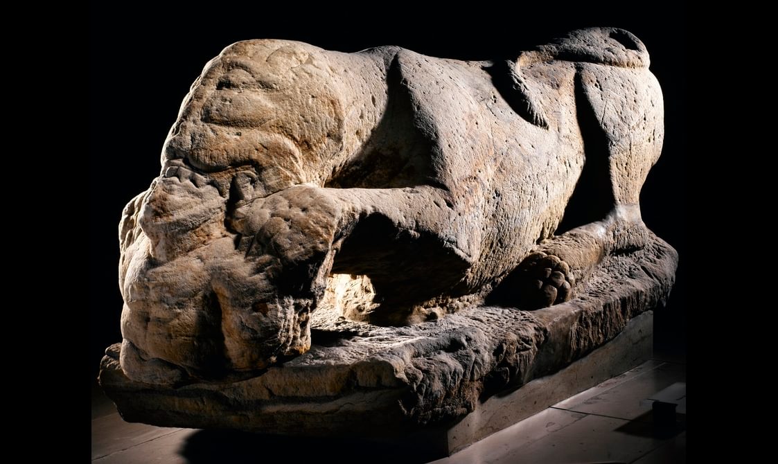 White sandstone carving of a ferocious lioness devouring the head and torso of a male figure.