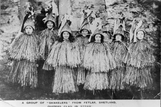 A black and white photograph of women dressed in tall coned decorative hats and flowing, straw like tops and skirts.