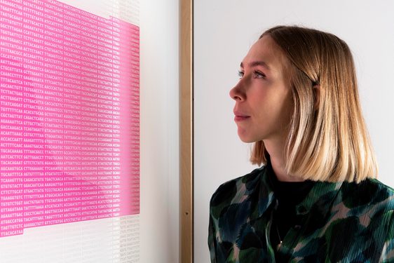 A person is looking at a framed picture. The picture looks like a square block of pink from a distance, but on closer inspection it's a stream of code for a virus.