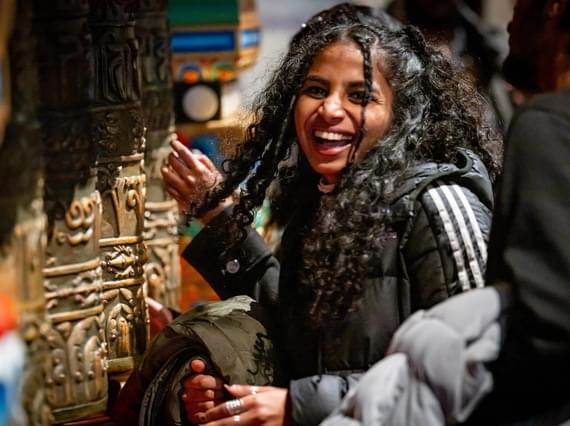A person standing smiling next to a set of prayer wheels.