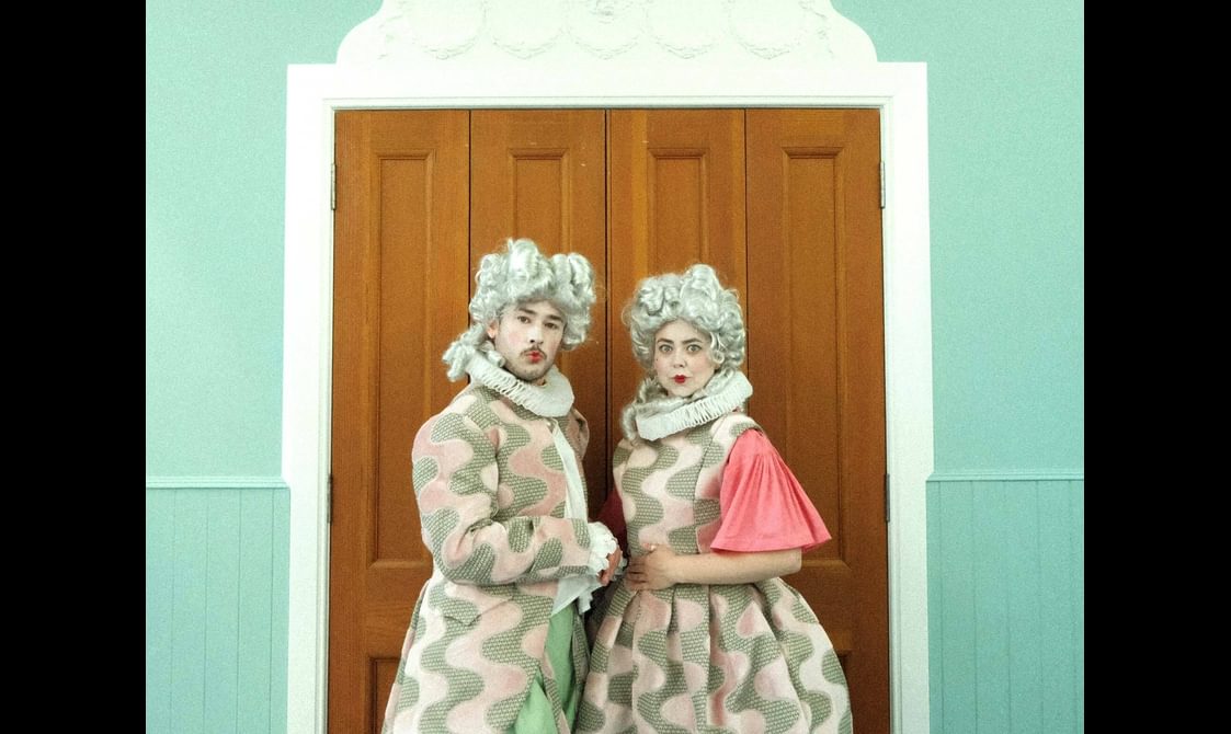 Two performers in regency dress wearing extravagant wigs.