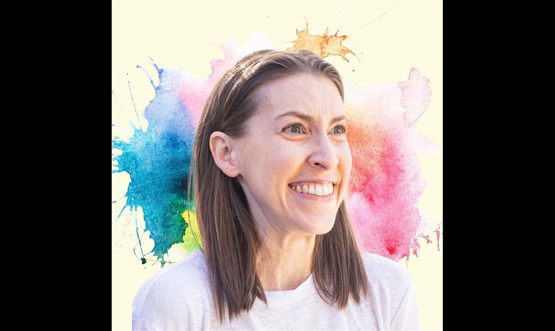 Eden Sher with short brown hair and a white t-shirt stands in front of a rainbow coloured graphic.