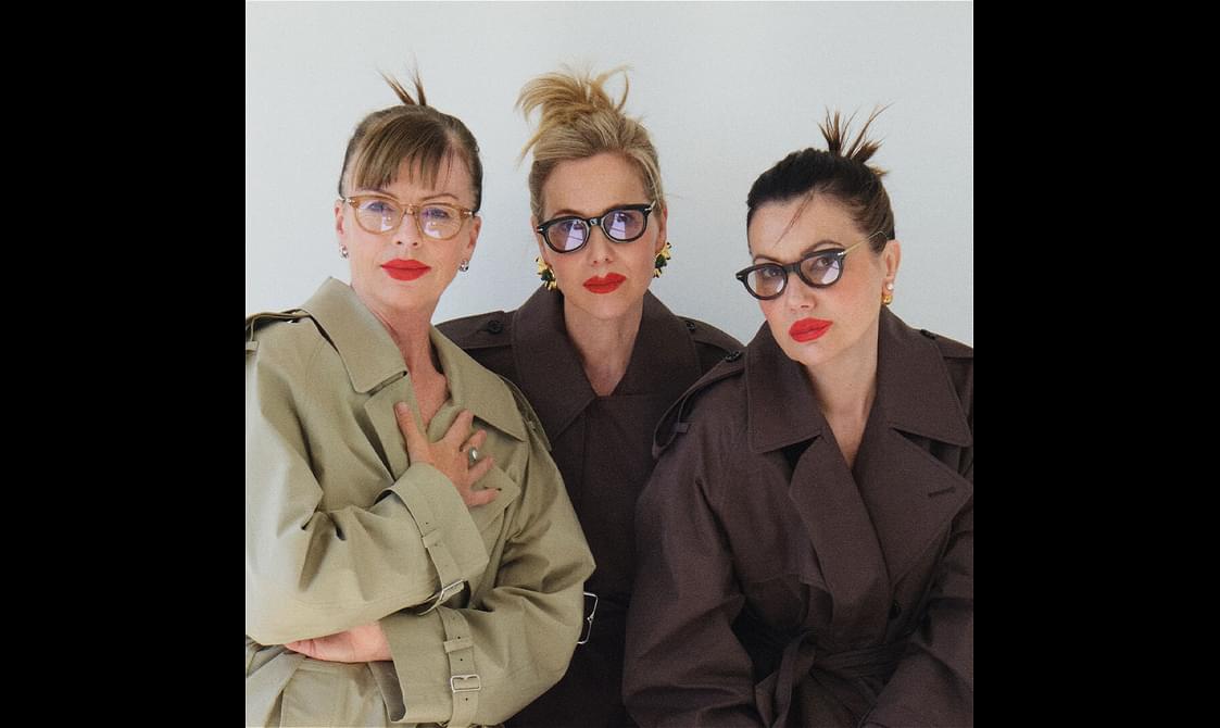 Three women in overcoats wearing glasses and red lipstick.