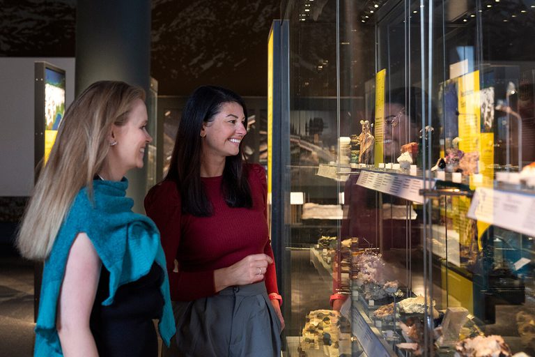 Two women looking at geological samples in a museum display case.