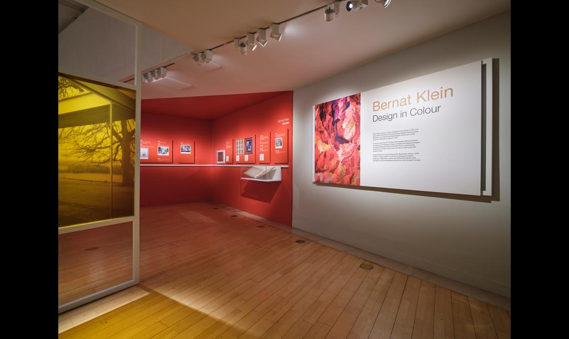 An exhibition room with a wall mounted information board titled, 'Bernat Klein Design in Colour'.