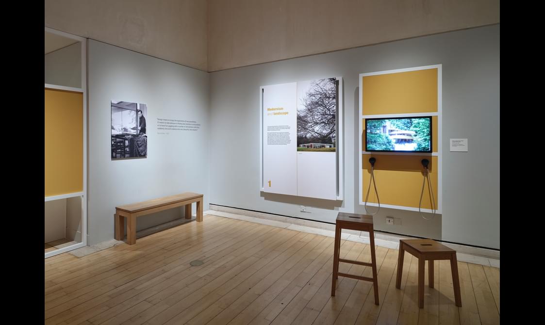 An exhibition room with a wall mounted information board, an audio-visual screen, and seating.