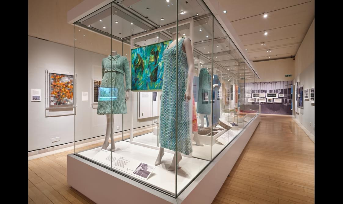 A glass exhibition case with and information board and 5 clothed mannequins.