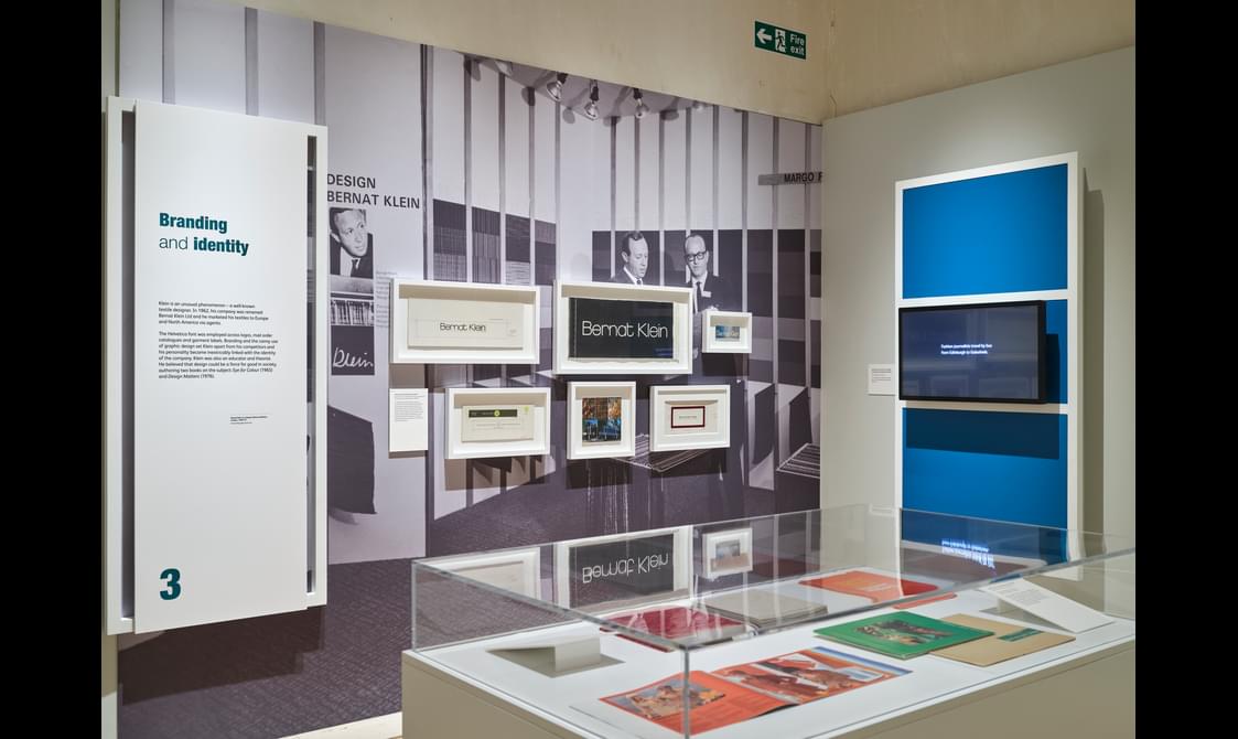 An exhibition room with a glass display case, screen and wall mounted information boards.