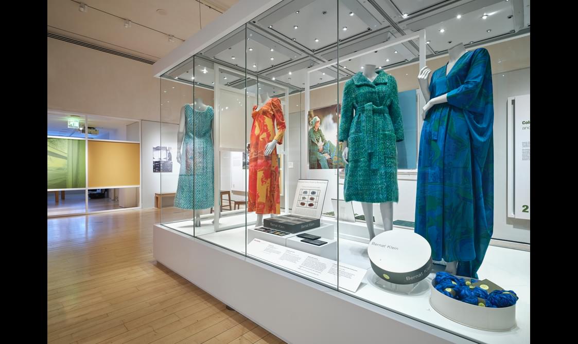 A glass exhibition case with and information board, material samples and 4 clothed mannequins.