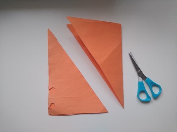 Two orange paper triangles lying on a flat surface with a blue scissors next to them.